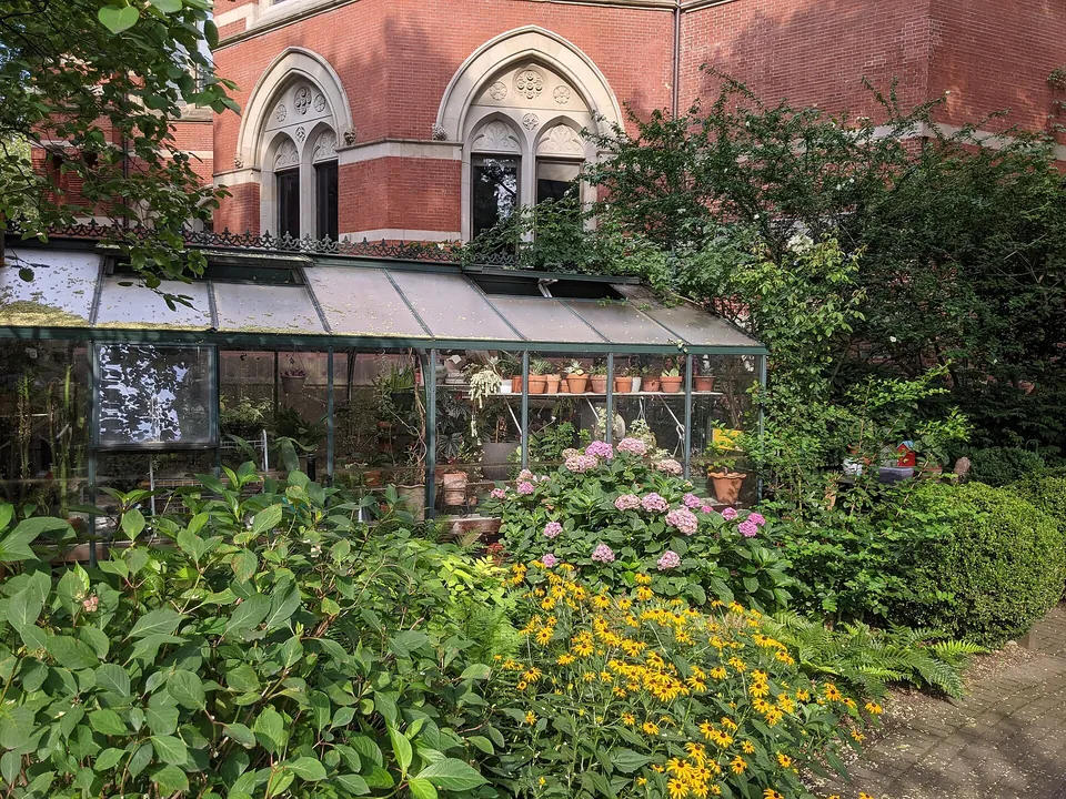 Gewächshaus mit Topfpflanzen inmitten eines blühenden Gartens